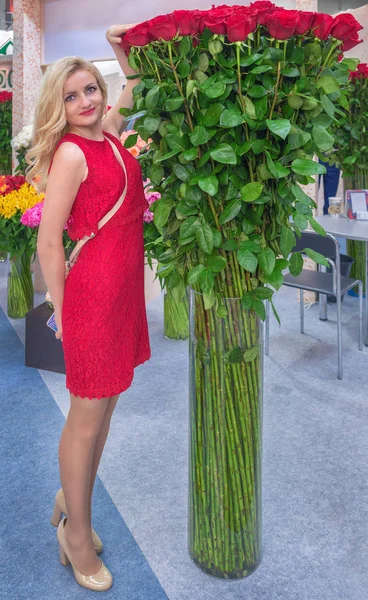 A young girl, blonde measures the height of a bouquet of red roses