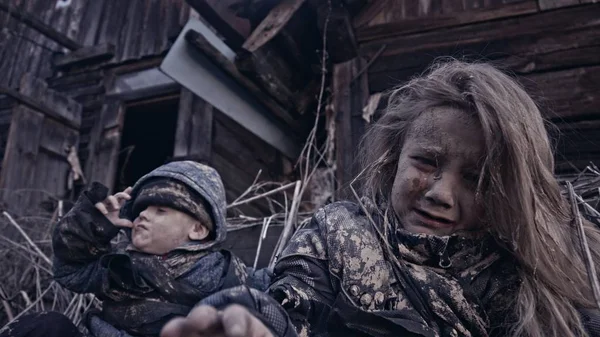 portrait of little dirty homeless orphans sitting and crying against abandoned building