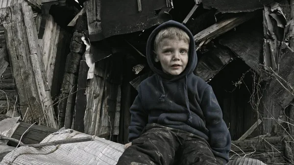 little sad orphan child sitting beside abandoned building