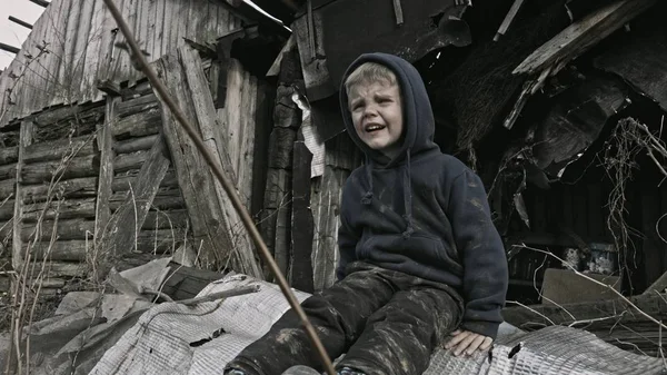 little homeless orphan boy crying beside abandoned building