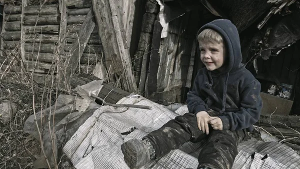 悲伤的无家可归的男孩坐在和令人沮丧的在废弃的村庄 — 图库照片