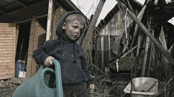 肮脏的孤独的男孩玩浇水罐在废弃的村庄 — 图库照片