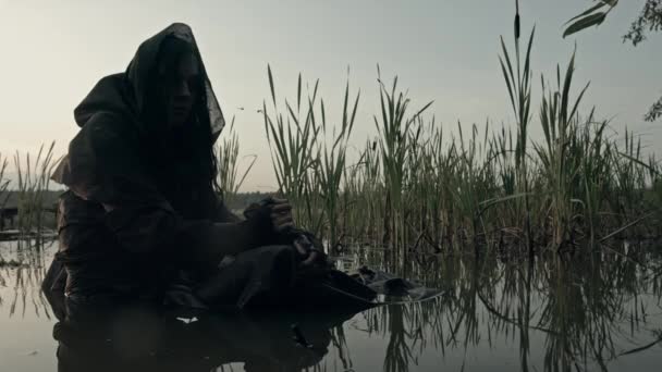 海岸の汚れた水の中に座っている古いコートの女性の概念 — ストック動画