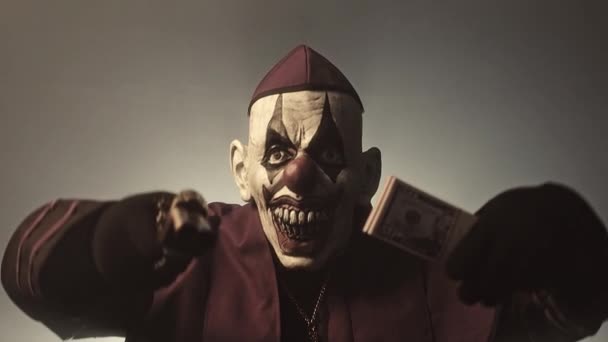 黑暗牧师在可怕的小丑面具摆姿势与钱和枪对灰色背景 — 图库视频影像