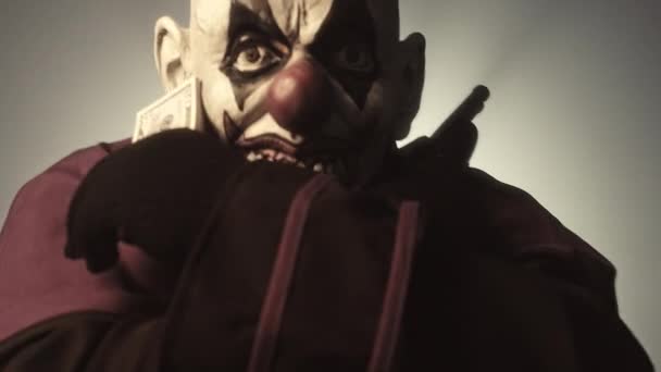 Темный Священник Страшной Клоунской Маске Позирует Деньгами Пистолетом Сером Фоне — стоковое видео
