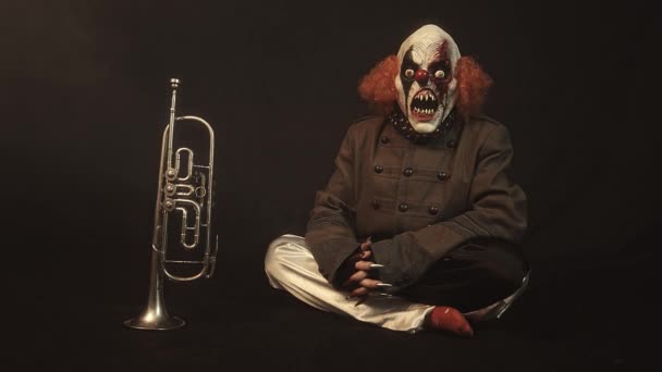 Enge Clown Zittend Naast Trompet Tegen Mistige Achtergrond — Stockvideo
