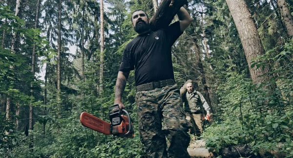 两个野蛮的高加索伐木工人拿着原木在森林里 — 图库照片