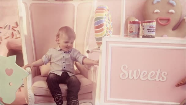 Маленький Белый Мальчик Сидит Кресле Позирует Перед Камерой Розовых Тонах — стоковое видео