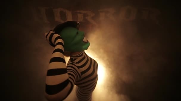Vrouwelijke Clown Groen Masker Gestreepte Kleding Poseren Tegen Mistige Achtergrond — Stockvideo