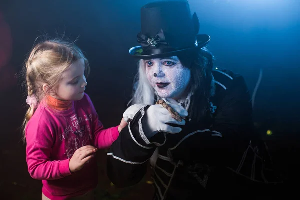 dark scary man in venetian costume and mask posing with snake and little girl against misty background