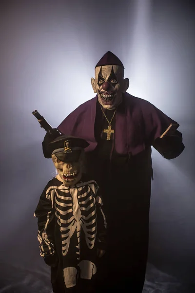 お金と灰色の背景に対して銃でポーズ怖いピエロのマスクとスケルトン少年で暗黒の司祭 — ストック写真