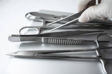 Hafif bir arka planda cerrahi aletler. Eldivenli el cerrahi forseps tutuyor. Tıbbi kıskaç, neşter, iğne tutacağı.