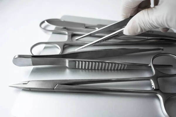 Hafif bir arka planda cerrahi aletler. Eldivenli el cerrahi forseps tutuyor. Tıbbi kıskaç, neşter, iğne tutacağı.