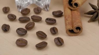 Cam bir tabaktan kahve taneleri döküldü. Yakındaki kokulu baharatlar - yıldız anason yıldız ve tarçın çubukları vardır. Eski ahşap bir yüzeyde.