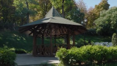 Dinlenmek için parkta ahşap çardak. Yeşil manzara. Ağaçların, çalıların ve çimenlerin sonbaharın başlarında. Sıcak bir gün.