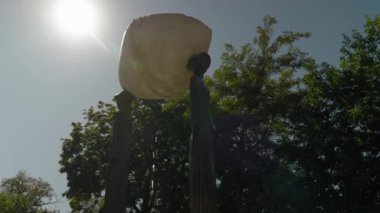 Çeşme. Rakamlar, suyun aktığı bir kase tutar. Parkta şelale. Su yavaş yavaş dökülür ve kuyuya düşer. Güneşli bir gün.