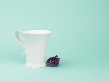 Turkuaz arka planda beyaz kupa ve leylaklar.