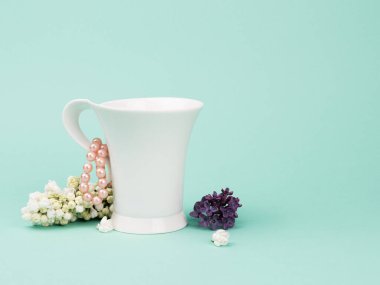 Beyaz Kupa, leylaklar ve turkuaz arka planda inci boncuklar..