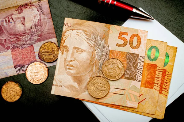 Real - BRL, money from Brazil. Money, Reais, Brazilian Real, Brazil. Folded money notes of the Brazilian Real in macro photography on a table with a red pen and coins in the scene