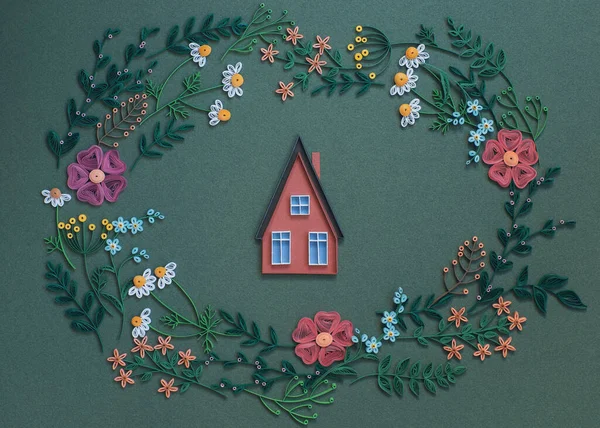 the house inside round frame with paper flowers and leaves isolated on a green paper background. Top view.  Hand made of paper quilling technique.