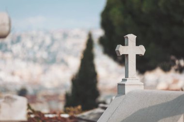 Zarif haç, sakin bir mezarlıkta tek başına duruyor. Uzak bir şehir manzarasına bakıyor. Öğleden sonra saatlerinde yumuşak güneş ışığıyla yıkanmış.