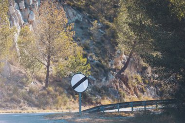 Curved road with no entry sign surrounded by scenic mountain landscape in bright daylight. A no entry sign stands at the curve of a road, framed by lush green trees and rocky cliffs 
