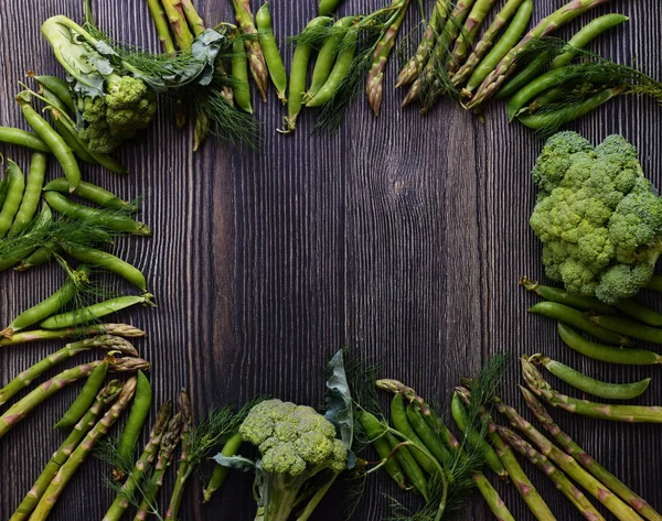 Frame with Fresh Green food, Green vegetables on wooden board. Composition on a dark wooden background of green organic vegetarian products: peas, dill, broccoli, asparagus. Top view.