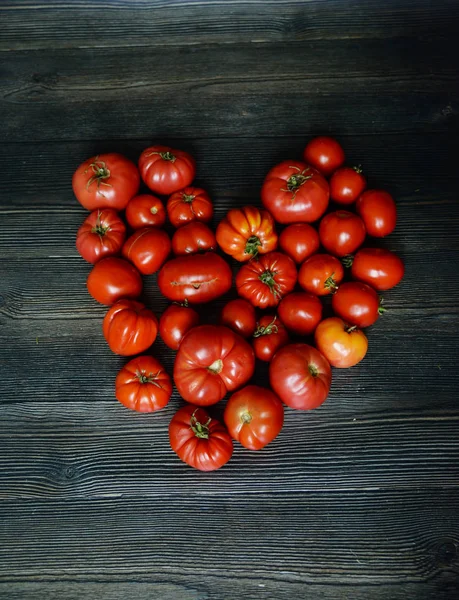 Domatesler eski masada. Kırmızı Gıda arka plan. Domates kalbi. Koyu ahşap arka plan üzerinde taze sebze üst görünümü. Eski bir rustik ahşap yüzeyüzerinde izole yatay kompozisyon