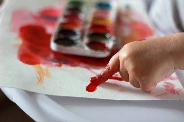 Photo child draws a finger in red paint on paper. hands in paint