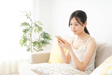 Genç Asyalı kadın evde akıllı telefon kullanıyor.