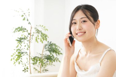 Genç Asyalı kadın evde akıllı telefon kullanıyor.