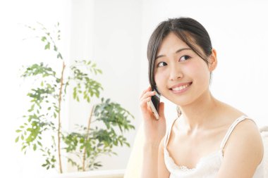 Genç Asyalı kadın evde akıllı telefon kullanıyor.