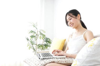 Genç mutlu Asyalı kadın evde bilgisayar kullanıyor. 