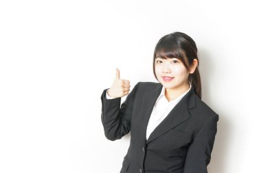 Takım elbiseli genç Asyalı kadın baş parmağını beyazın üstünde gösteriyor.