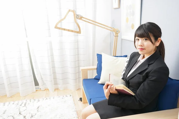 穿着西服的年轻亚洲女人坐在沙发上看书 — 图库照片