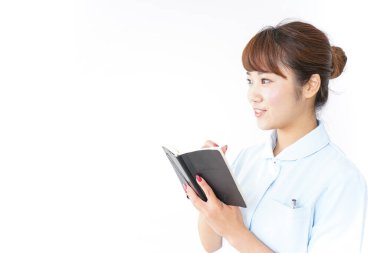 Genç Asyalı hemşire beyaz arka planda not defteri tutuyor.