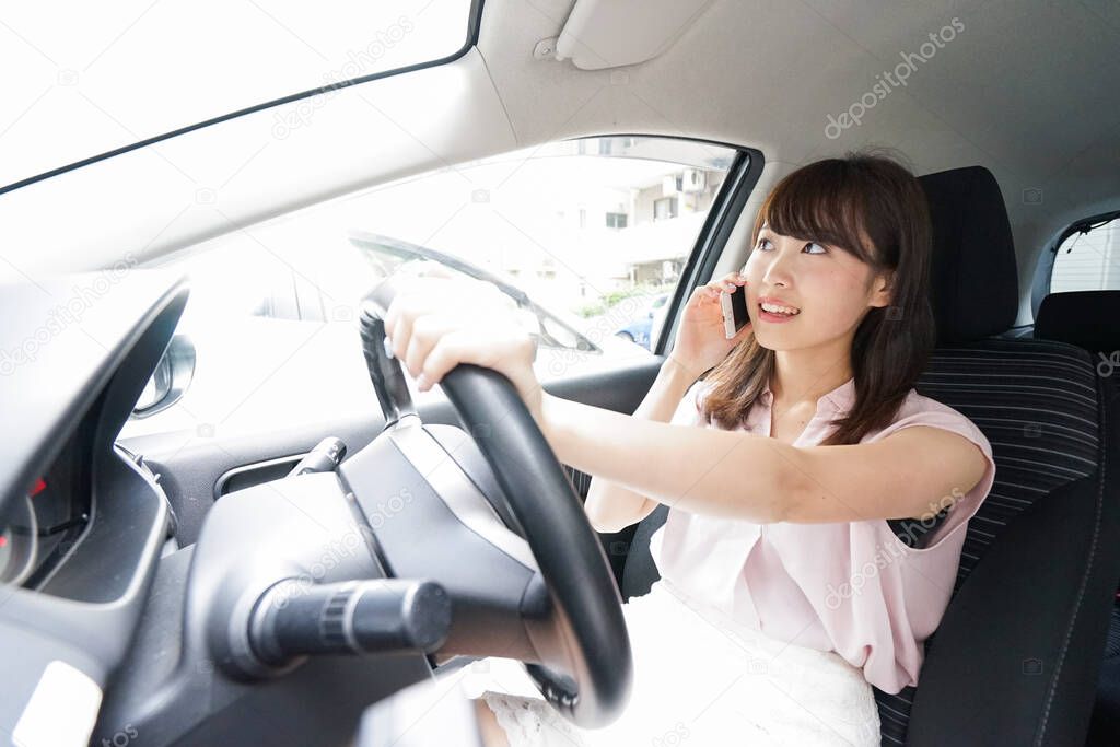 Driving young asian woman using smartphone