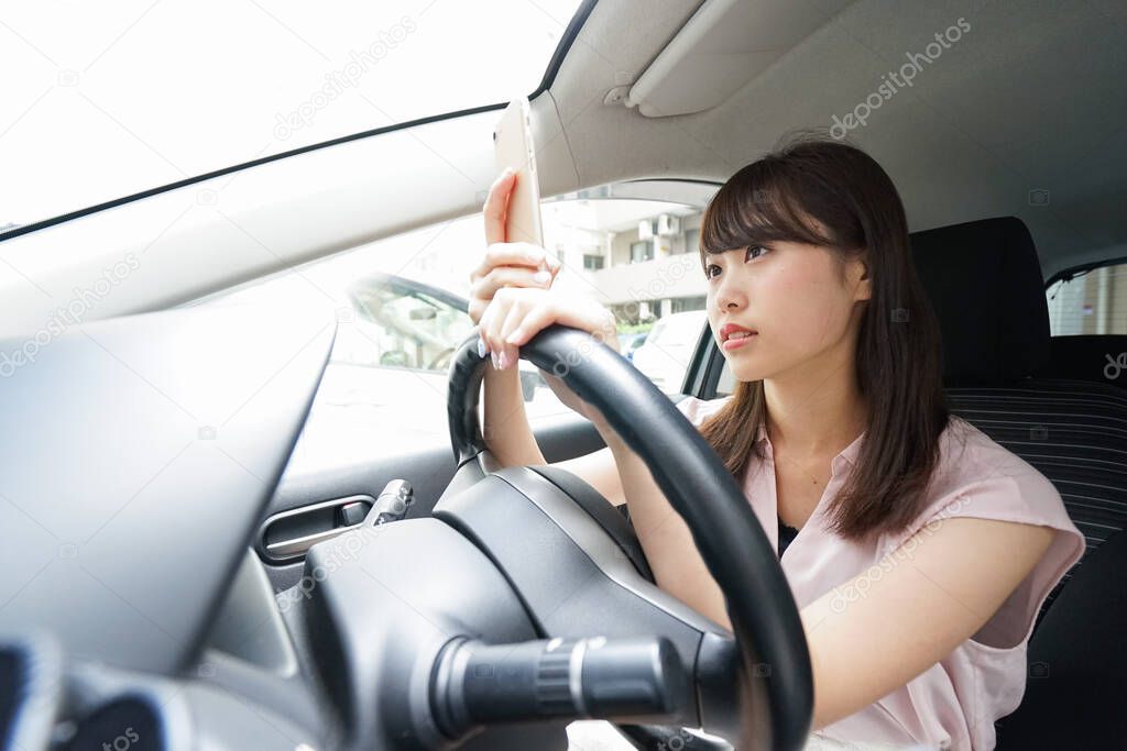 Driving young asian woman using smartphone