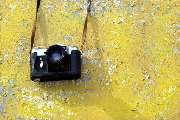 Vintage câmera velha pesa em uma cinta no fundo de uma antiga parede amarela — Fotografia de Stock