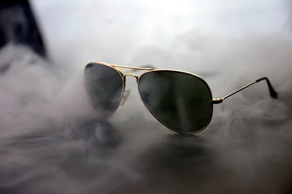 Okulary przeciwsłoneczne na tle czerni oraz light w dym, za kulisami — Zdjęcie stockowe