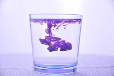 Glass with water on a white background with purple paint. clipart