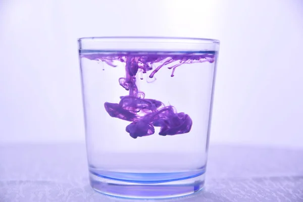 Glass with water on a white background with purple paint.
