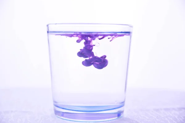 Vidro Com Água Sobre Fundo Branco Com Tinta Roxa — Fotografia de Stock