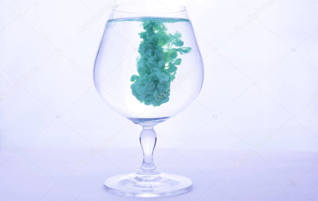 green paint in water in a crystal glass on a white background.