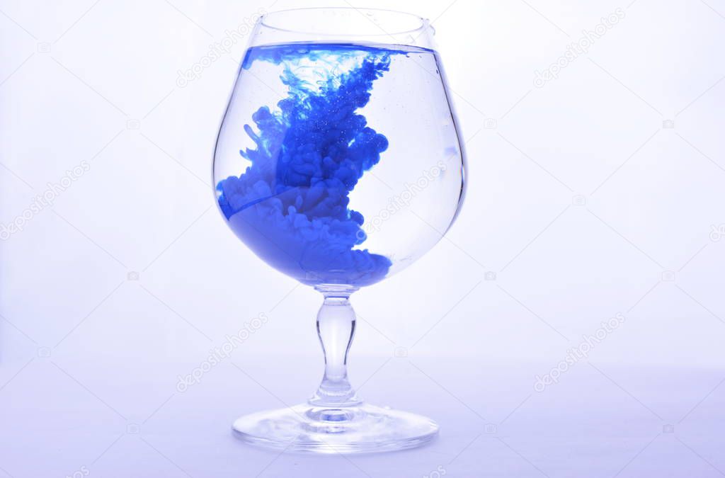 Blue paint in water in a crystal glass on a white background.