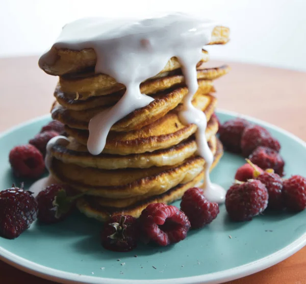 Pannkaka med rinnande yoghurt på en blå tallrik med hallon — Stockfoto