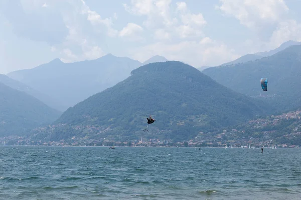 Lago de Como, Italia - 21 de julio de 2019. Deportes acuáticos: kitesurfer está haciendo un truco en el aire en un día de verano soleado brillante cerca del Colico, ciudad en Italia. Montañas Alp en el fondo. Kiteboarding, extremos s — Foto de Stock