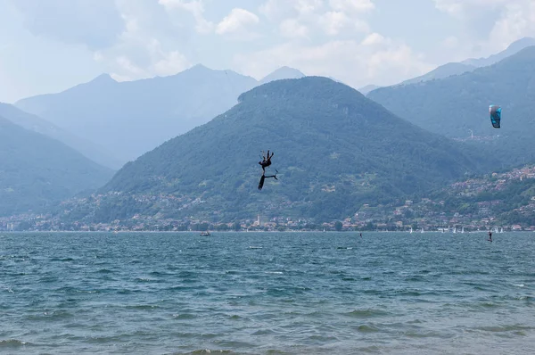 Lago de Como, Italia - 21 de julio de 2019. Deportes acuáticos: kitesurfer está haciendo un truco en el aire en un día de verano soleado brillante cerca del Colico, ciudad en Italia. Montañas Alp en el fondo. Kiteboarding, extremos s — Foto de Stock