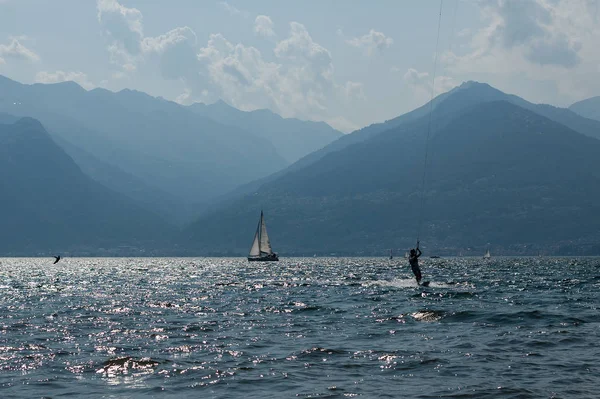 Como Gölü, İtalya - 21 Temmuz 2019. Su sporları: Kitesurfer Colico, İtalya'da kasaba yakınında güneşli bir yaz gününde dalgalar ve tekne rüzgar sörf. Arka planda Alp dağları.