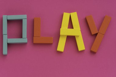 Çok renkli tahta tuğlalardan yapılmış Kelime Oyunu. Mor kağıt üzerinde oyuncaklar. Çocuk oyunu konsepti. Pembe arka planda parlak kırmızı, sarı, mavi renkler. Üst manzara, düz uzanma